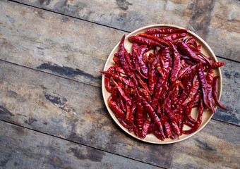 Red hot dry chili peppers in wooden bowl on wood background, top view