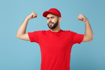 Delivery man in red uniform workwear isolated on blue wall background, studio portrait. Professional male employee in cap t-shirt print working as courier dealer. Service concept. Mock up copy space.