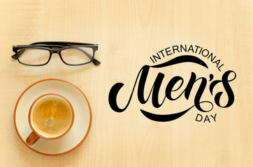 Desktop with notebook, pencil, eyeglasses and coffee cup. Hand sketched International Men's day text.