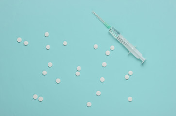 Minimalistic medical still life. Pills and syringe on a blue background. Top view