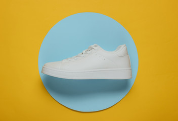 Stylish white sneaker on a yellow background with blue circle in the middle. Top view. Minimalism fashion still life