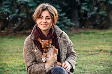 young woman in coat holds a small dog toy Terrier in her arms in autumn.