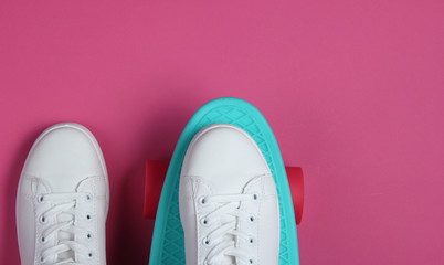 Stylish white sneakers with cruiser board on pink background. Summertime fun. Studio shot, top view.