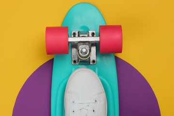 Stylish white sneakers with cruiser board on colored background. Summertime fun. Studio shot, top view.