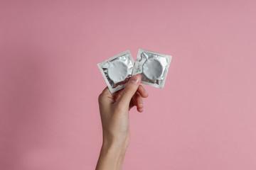 Female hand holding condom on pink background. Top view. The concept of sexual preservation - obrazy, fototapety, plakaty