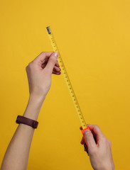 Female hands take measurements with industrial tape measure on yellow background