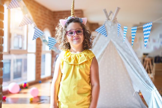 Beautiful toddler wearing glasses and unicorn diadem standing and smiling at kindergarten