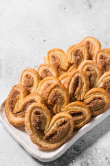 Puff pastry with sugar and cinnamon in a white ceramic plate on a light gray table