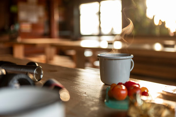 Grey enamel cup of hot steaming coffee or tea sitting on an old table in a mountain shelter.
