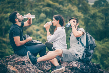Group of hiking people sitting on rock and drinking water after reach top of mountain, hiker doing adventure activity in summer to walk in a forest and climbing. Exploration natural and see top view