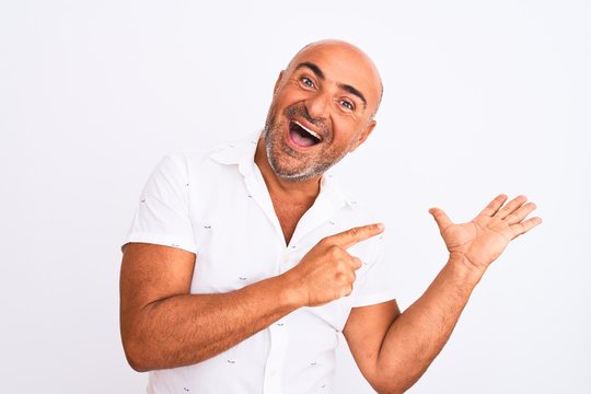 Middle age handsome man wearing elegant shirt standing over isolated white background amazed and smiling to the camera while presenting with hand and pointing with finger.