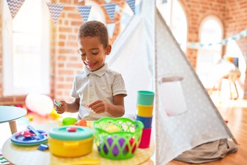 Beautiful african american toddler playing with plastic food and cutlery toy at kindergarten