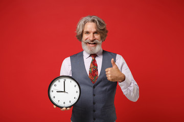 Cheerful elderly gray-haired mustache bearded man in classic shirt vest and tie isolated on red...