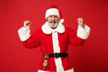 Fototapeta na wymiar Joyful elderly gray-haired mustache bearded Santa man in Christmas hat posing isolated on red background. Happy New Year 2020 celebration holiday concept. Mock up copy space. Doing winner gesture.