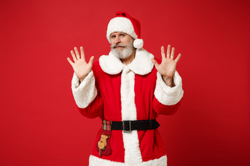 Fototapeta na wymiar Elderly gray-haired mustache bearded Santa man in Christmas hat posing isolated on red background. Happy New Year 2020 celebration holiday concept. Mock up copy space. Rising hands, showing palms.