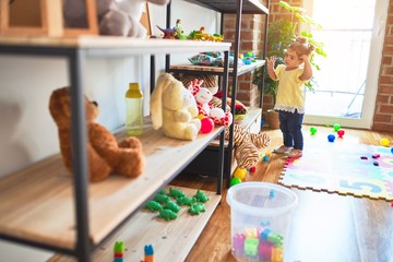 Beautiful toddler standing taking toys of shelving at kindergarten