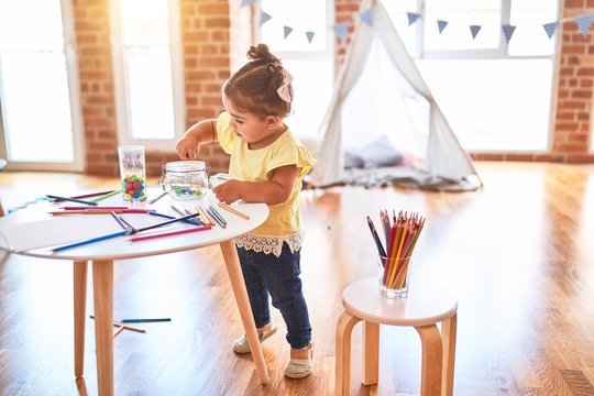Beautiful toddler standing playing with chocolate colored balls on the table at kindergarten