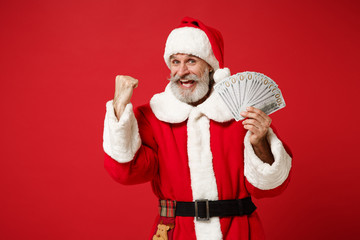 Fototapeta na wymiar Elderly gray-haired mustache bearded Santa man in Christmas hat isolated on red background. New Year 2020 celebration holiday concept. Mock up copy space. Hold fan of cash money, doing winner gesture.