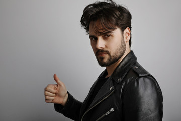 Studio close up portrait of young bearded hipster looking at the camera and showing OK with his hand.