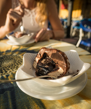 Traditional Calabrian Tartufo ice cream in cross-section with nougat filling at a cafe in Pizzo, woman sitting and eating a dessert in the background