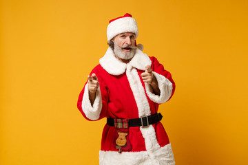 Fototapeta na wymiar Elderly gray-haired mustache bearded Santa man in Christmas hat posing isolated on yellow background. New Year 2020 celebration holiday concept. Mock up copy space. Pointing index fingers on camera.