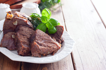 sliced baked beef fillet on a white dish with fresh herbs, horizontal, copy space