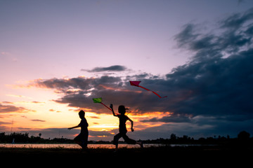 The little boy was playing kite at the park in the evening with sunset and silhouette.
