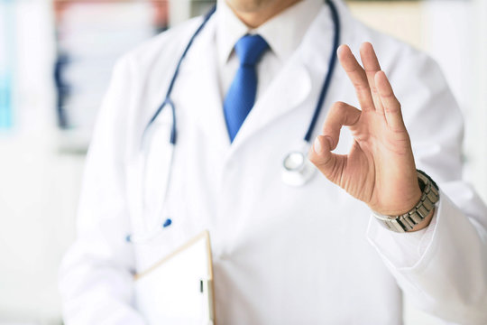 Close up of male doctor in white coat showing ok hand sign.