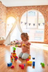 Beautiful blond toddler girl playing with plastic blocks to build a tower at kindergarten