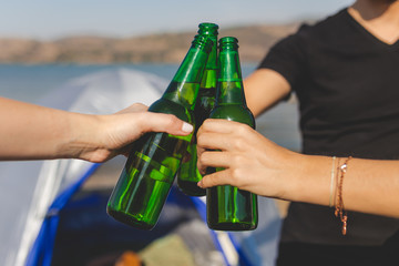 Friends clinking bottles of beer on beach camping picnic.