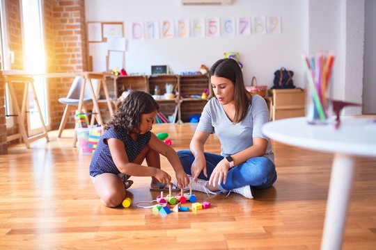 Beautiful teacher and toddler girl playing with train at kindergarten
