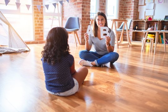 Beautiful teacher teaching alphabet to student toddler girl at kindergarten