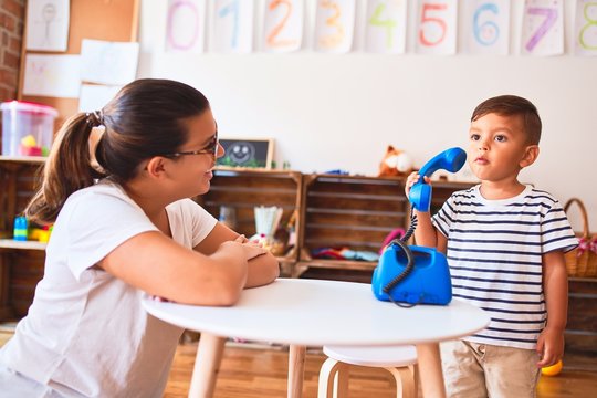 Beautiful teacher and toddler boy playing with vintage blue phone at kindergarten