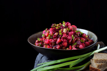 Vinaigrette salad with boiled vegetables in a clay bowl against the black background. Russian cuisine meal