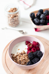Breakfast with yogurt, berries and granola on a light background.