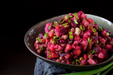 Vinaigrette salad with boiled vegetables in a clay bowl against the black background. Russian cuisine meal