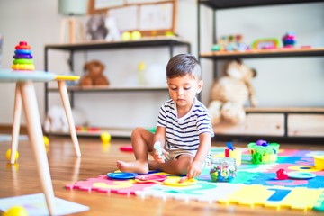 Beautiful toddler boy sitting on puzzle playing meals with plastic plates, fruits and vegetables at kindergarten