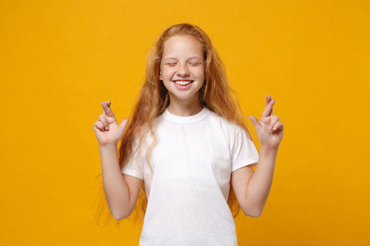 Pretty little ginger kid girl 12-13 years old isolated on yellow background. Childhood lifestyle concept. Mock up copy space. Wait for special moment keeping fingers crossed eyes closed, making wish.