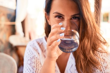 Young beautiful woman sitting at restaurant enjoying summer vacation drinking a glass of water - Powered by Adobe