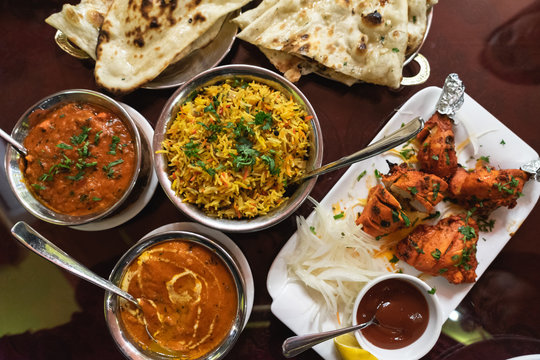 Assortment of Indian dishes for dinner, butter chicken, tikka masala, rice and naan