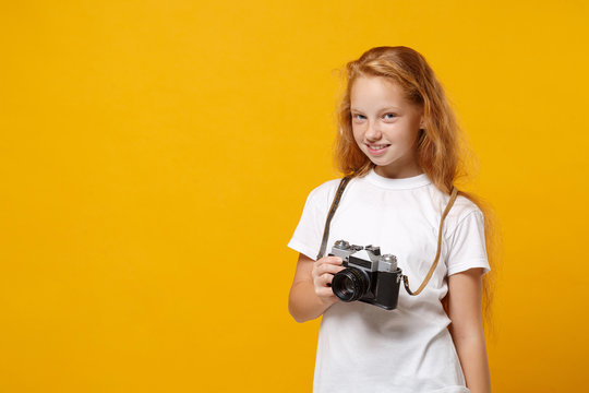 Smiling little ginger kid girl 12-13 years old in white t-shirt isolated on yellow wall background children portrait. Childhood lifestyle concept. Mock up copy space. Hold retro vintage photo camera.