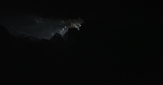 Reveal of two explorers entering a cave in slow motion with lights and smoke