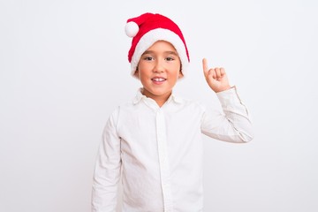 Beautiful kid boy wearing Christmas Santa hat standing over isolated white background showing and pointing up with finger number one while smiling confident and happy.
