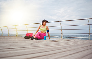 Young fit woman in sportwear sitting on a mat and resting on the beach