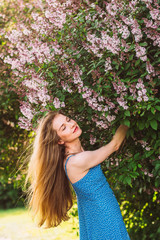 Portrait of smiling girl with blond hair and closed eyes and blue dress among lilac