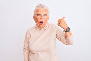 Senior grey-haired woman wearing turtleneck sweater standing over isolated white background Surprised pointing with hand finger to the side, open mouth amazed expression.