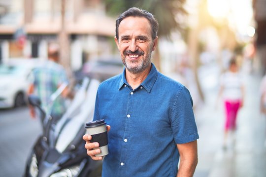 Middle age handsome man standing on the street drinking take away coffee smiling