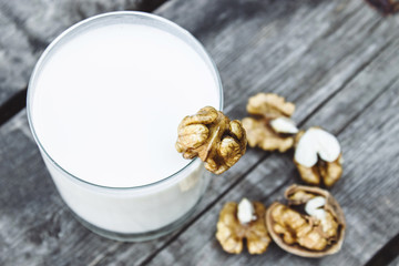A glass of white milk and walnuts on an old wooden table. Vegan milk from walnuts. Eco food.