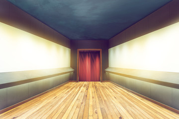 empty hallway of room with wooden floor and blank frame on the wall and a red curtain at the door, room behind walkway to the theater stage