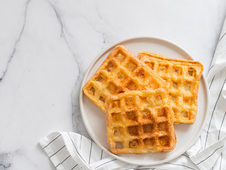 Perfect savory keto waffles. Two ingredients chaffles on plate over white marble background. Eggs and parmesan cheese low carb waffles. Top view or flat lay. Copy space for text or design.